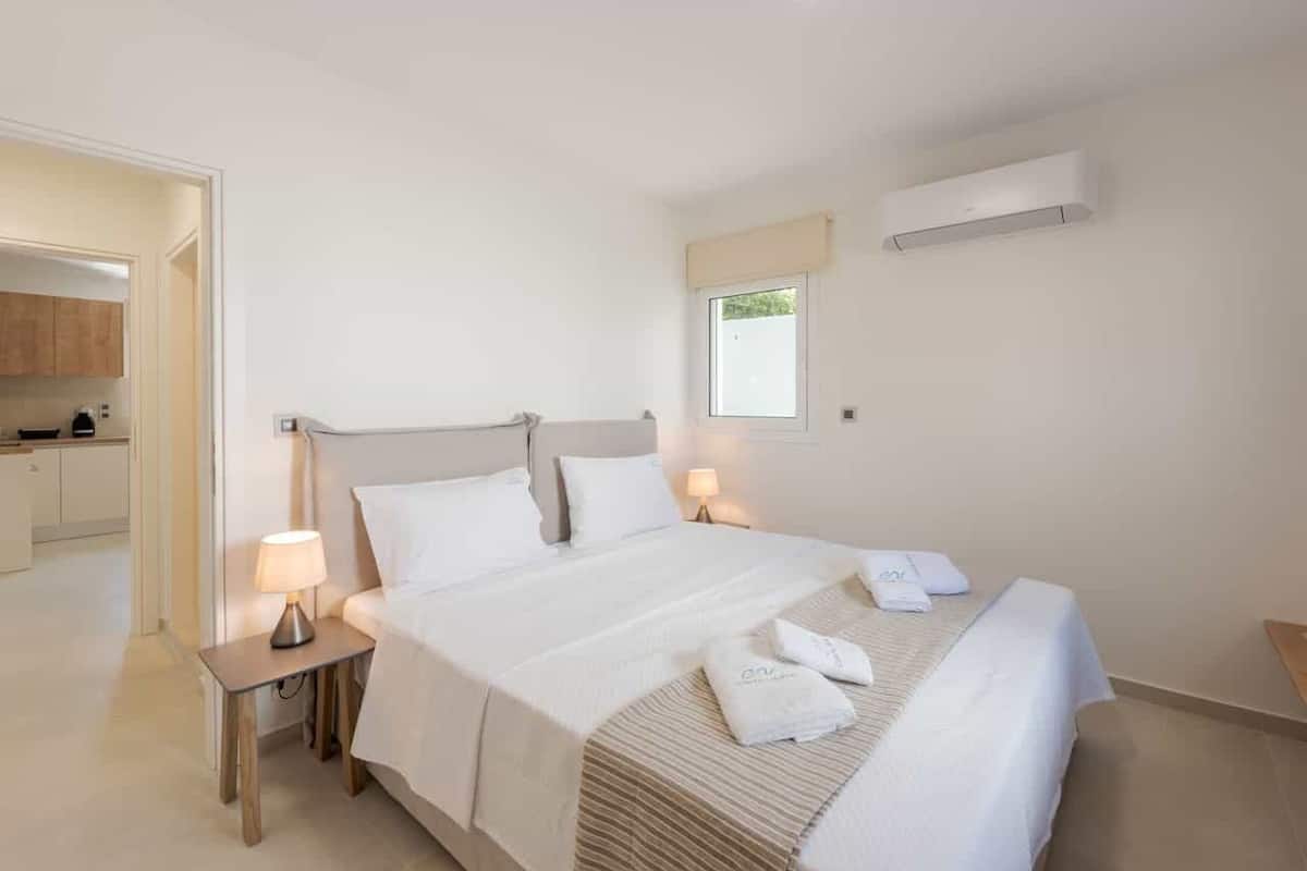 Una habitación de hotel con una cama grande, mesitas de noche con lámparas, una ventana y un aire acondicionado.