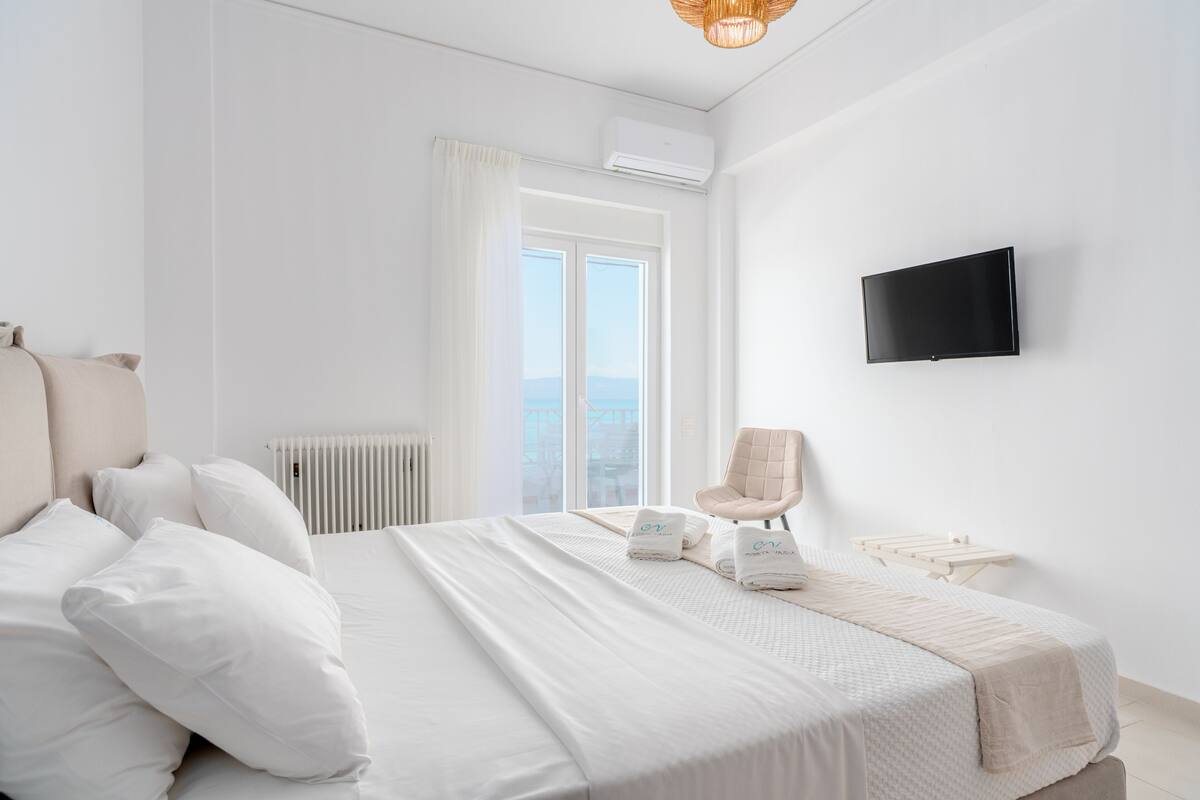 Una habitación de hotel moderna con una cama, una silla, un televisor y un ventanal con cortinas.
