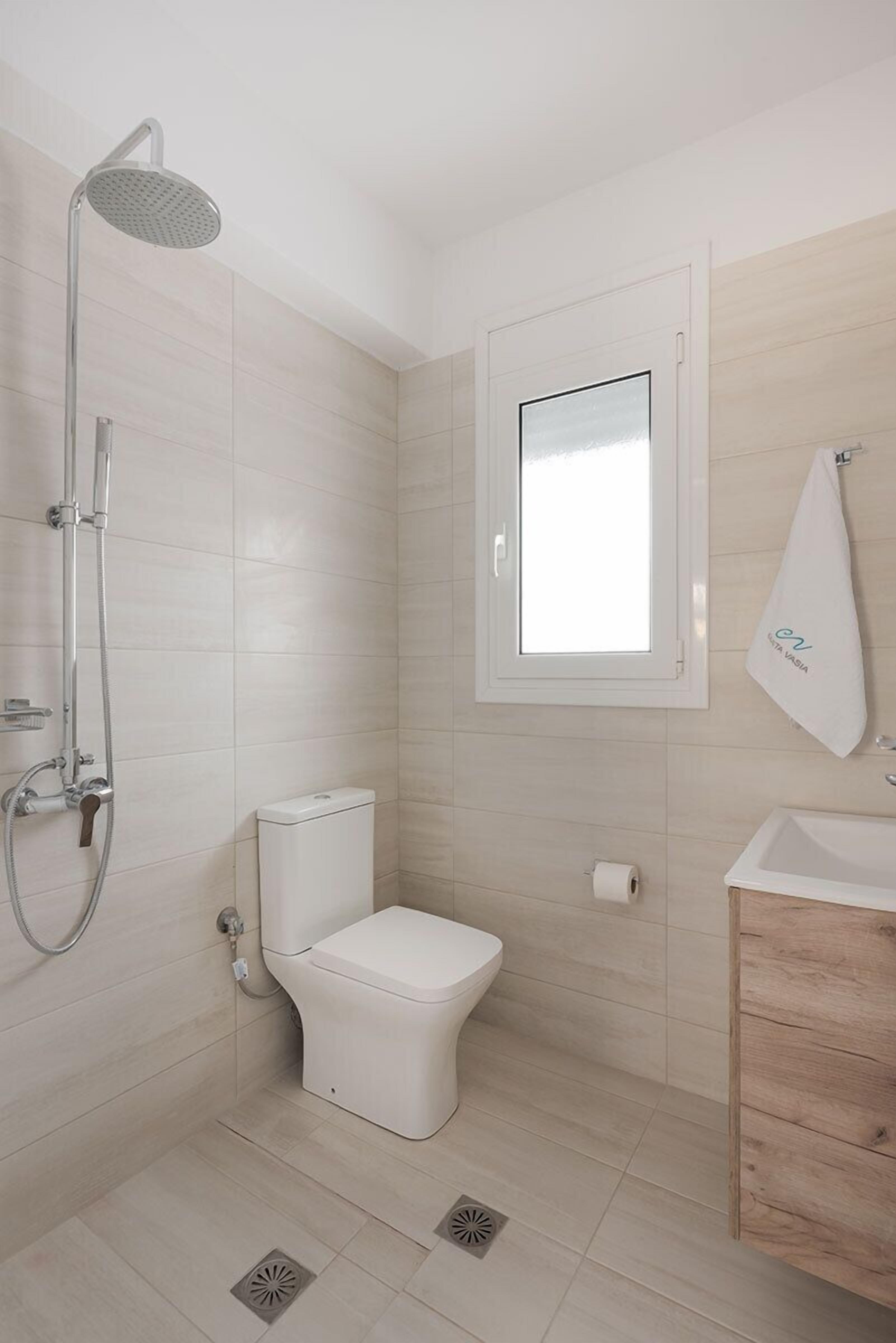 A bathroom with a shower, toilet, sink, and a window.