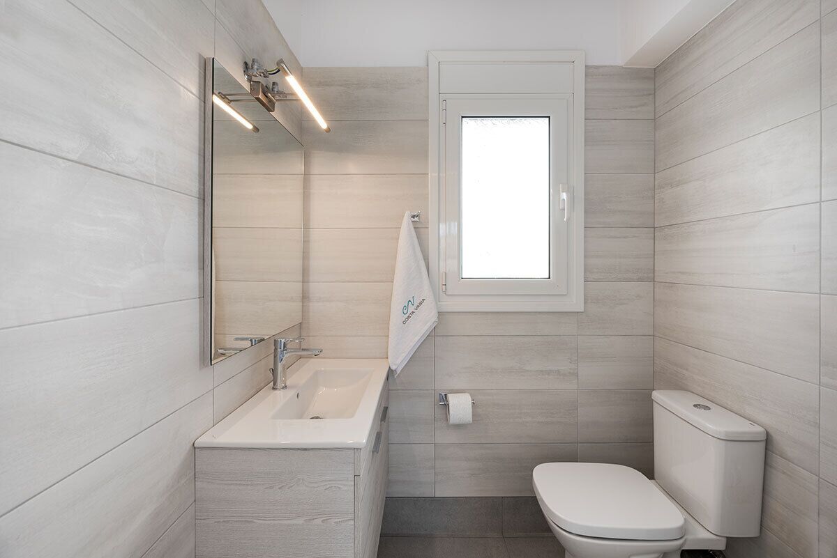 A modern bathroom with a wooden wall design, a white sink, a toilet, and a window providing natural light.