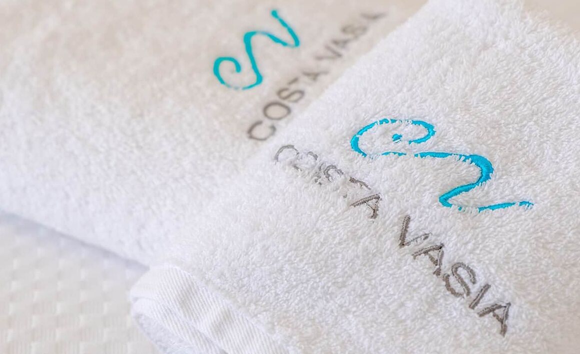 Una toalla blanca con bordado del texto "COSA VASIA" y un logotipo.