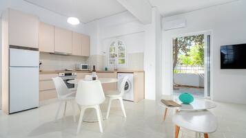 A modern kitchen with white appliances, a dining area with white chairs, and a view of greenery outside.