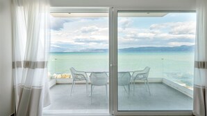 Een balkon met een glazen deur, witte stoelen en uitzicht op zee en bergen.