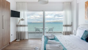 Een hotelkamer met een groot bed, een televisie, een bureau met stoelen en uitzicht op zee.