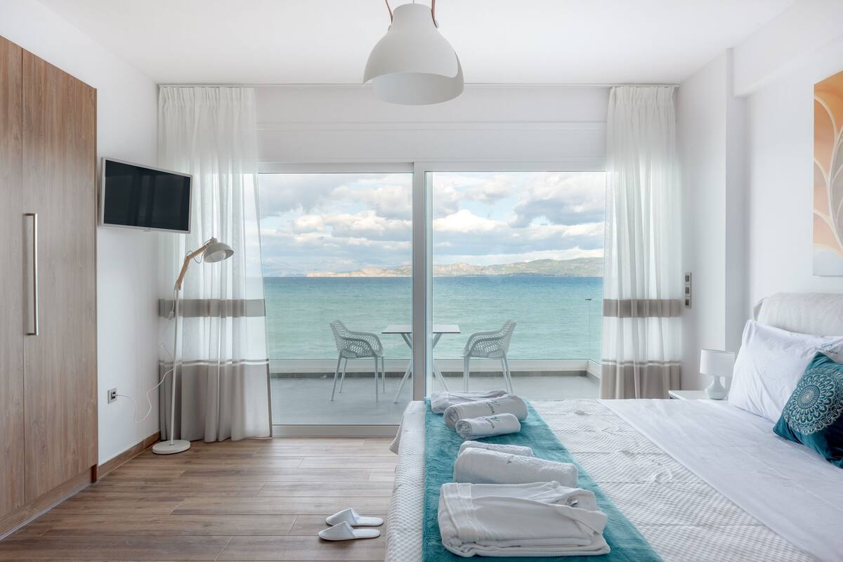 Habitación de hotel con una cama grande, televisión, escritorio con sillas y vista al mar.