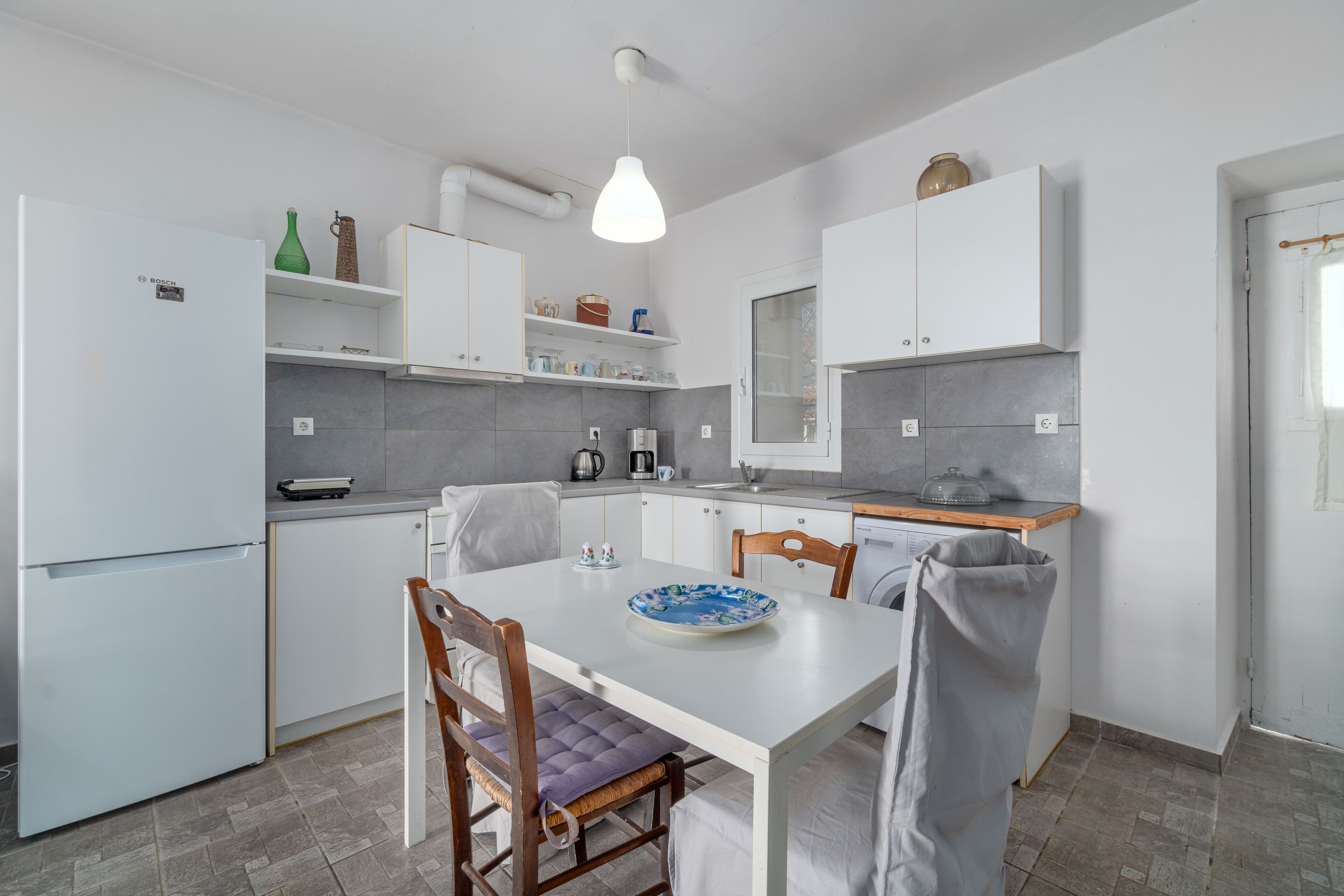 A compact kitchen with white cabinets, a dining table, and a hanging light fixture.
