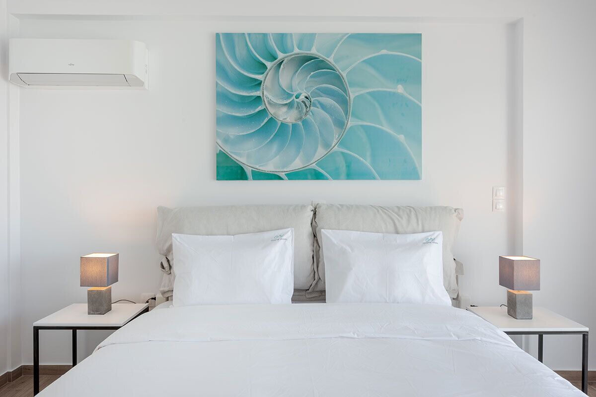 Ein Schlafzimmer mit einem Bett, zwei Nachttischen, einer Wand-Klimaanlage und einem großen, abstrakten Gemälde.