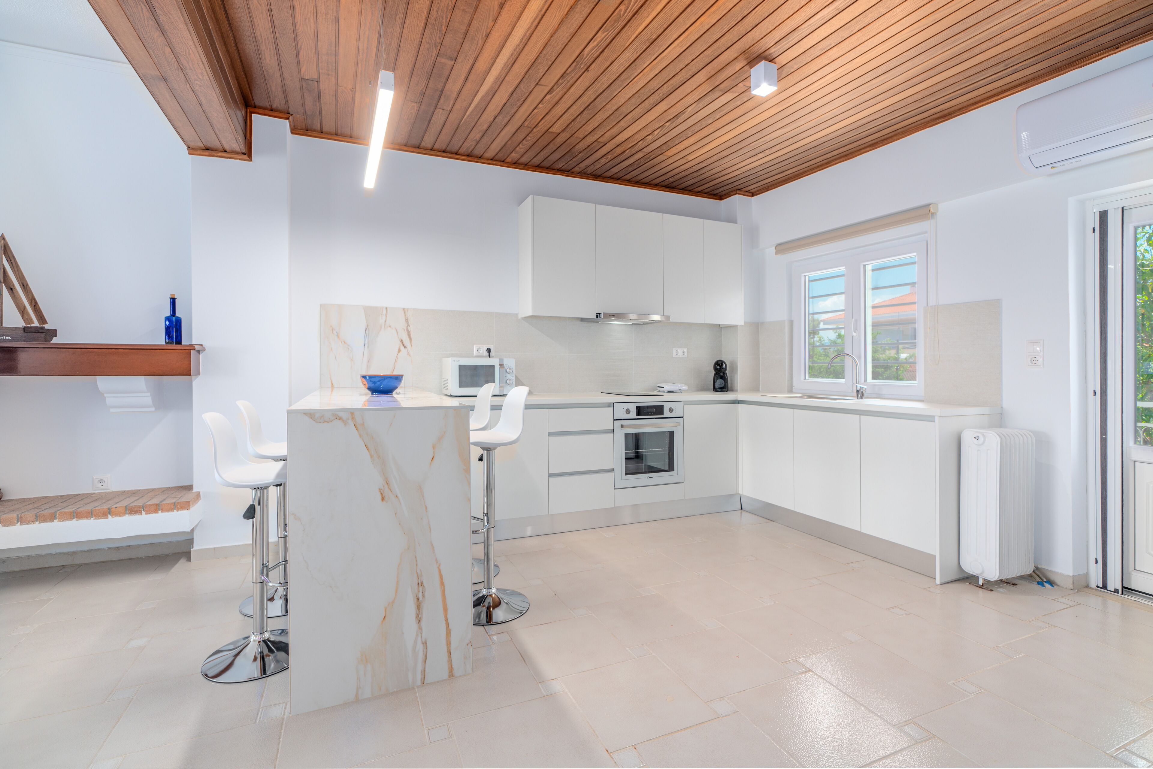 A modern kitchen with white cabinets, a marble island, and two white bar stools.