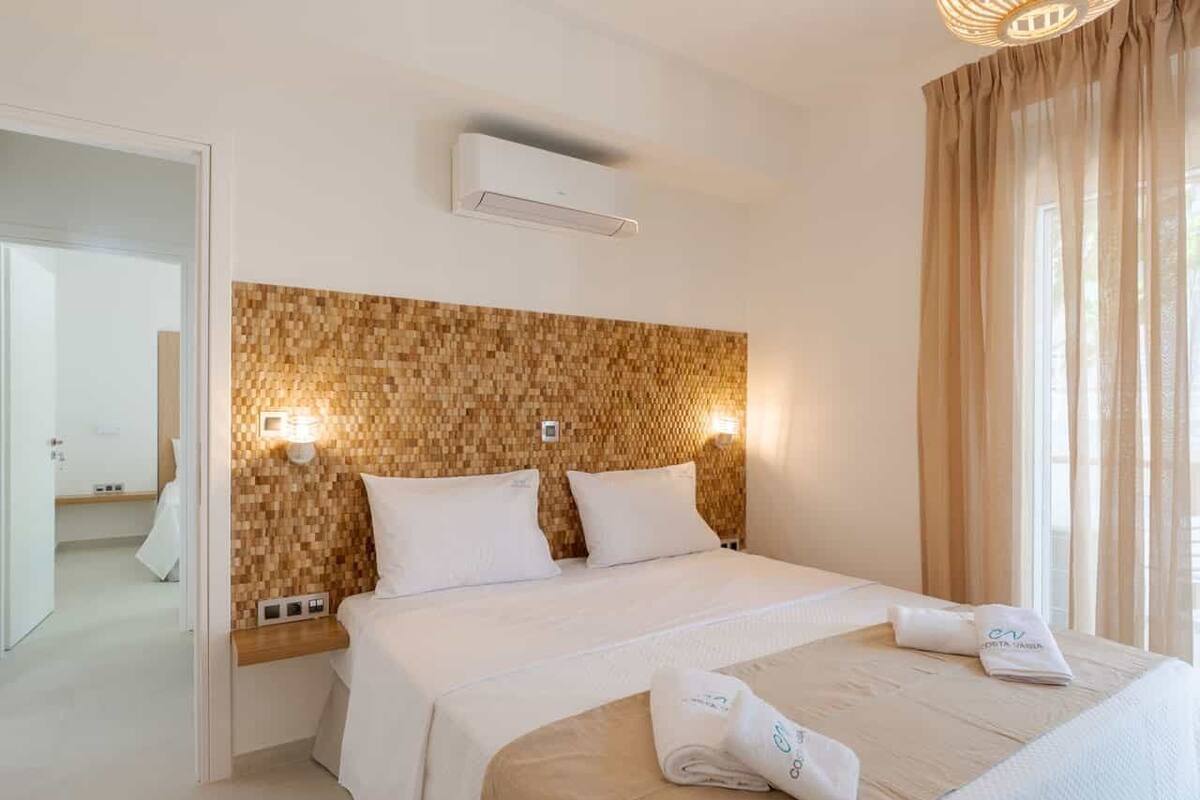 Una habitación de hotel con una cama grande, un cabecero de madera, dos mesitas de noche y una ventana con cortinas.
