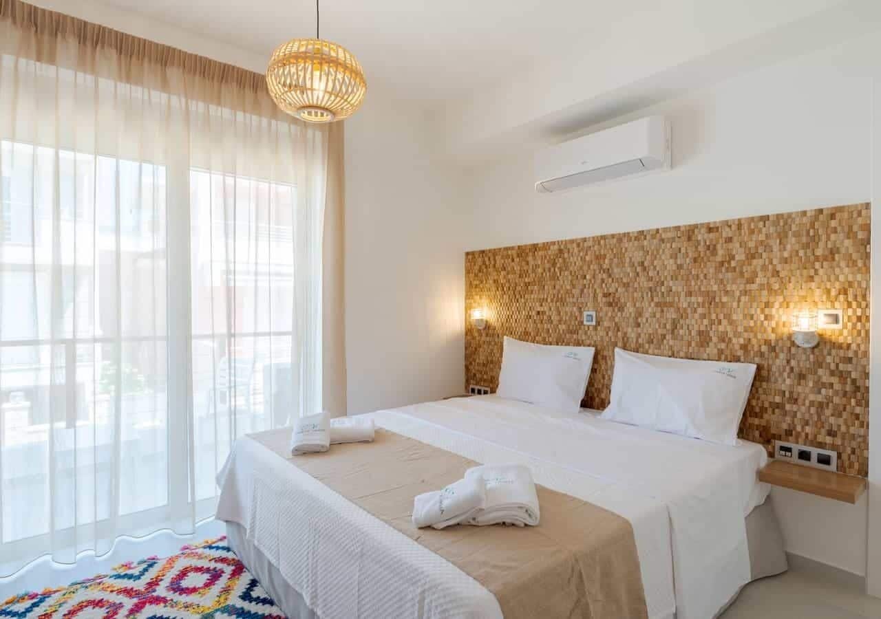 A hotel room with a large bed, a woven headboard, a window with sheer curtains, and a colorful rug.