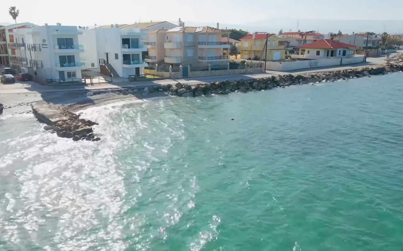 A coastal residential area with multi-story buildings, a rocky shoreline, and clear turquoise water.