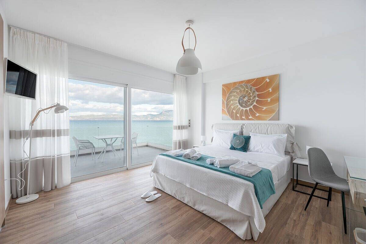 Una habitación de hotel moderna con una cama grande, un escritorio, una silla, un televisor y un balcón con vistas al mar.