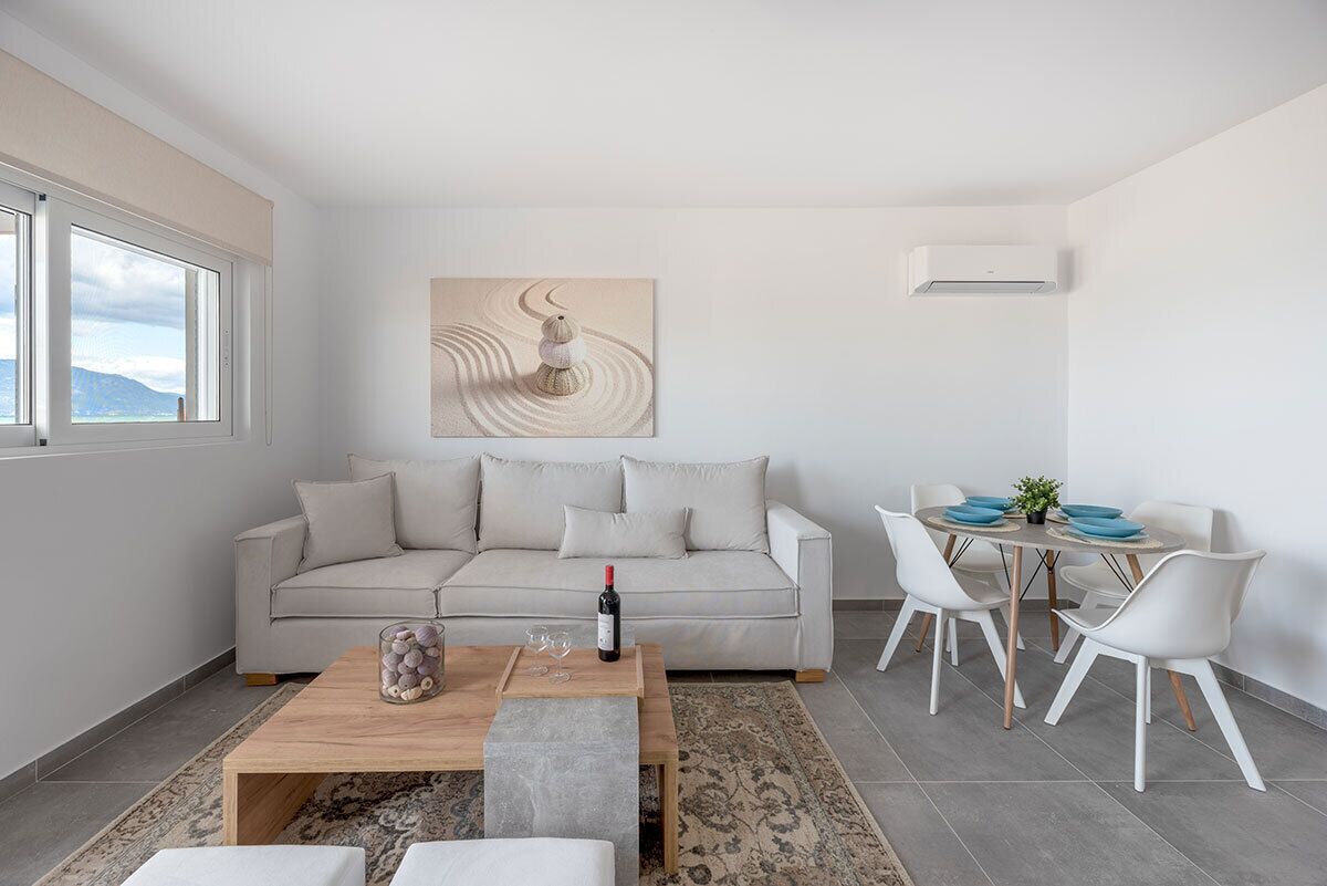 A modern living room with a beige sofa, a wooden coffee table, and a dining area with white chairs and a round table.