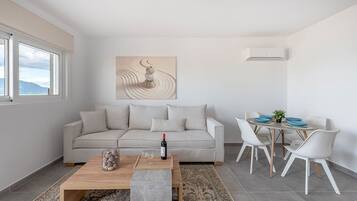 A modern living room with a beige sofa, a wooden coffee table, and a dining area with white chairs and a round table.
