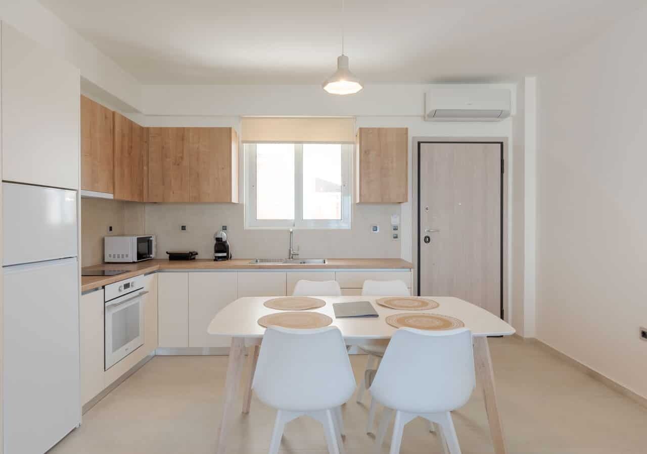 Une cuisine moderne avec des meubles blancs, une table à manger avec quatre chaises et une fenêtre au-dessus de l’évier.