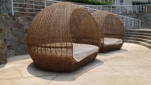 Two wicker swing chairs with cushions, positioned on a stone-paved area with a stone wall and metal railing in the background. - Apatel The Mansion Jasmine Aurora 31 I (Jakarta)