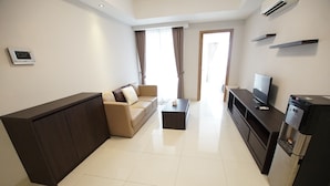 A modern living room with a sofa, a coffee table, a TV, and a refrigerator. - Apatel The Mansion Jasmine Aurora 31 I (Jakarta)