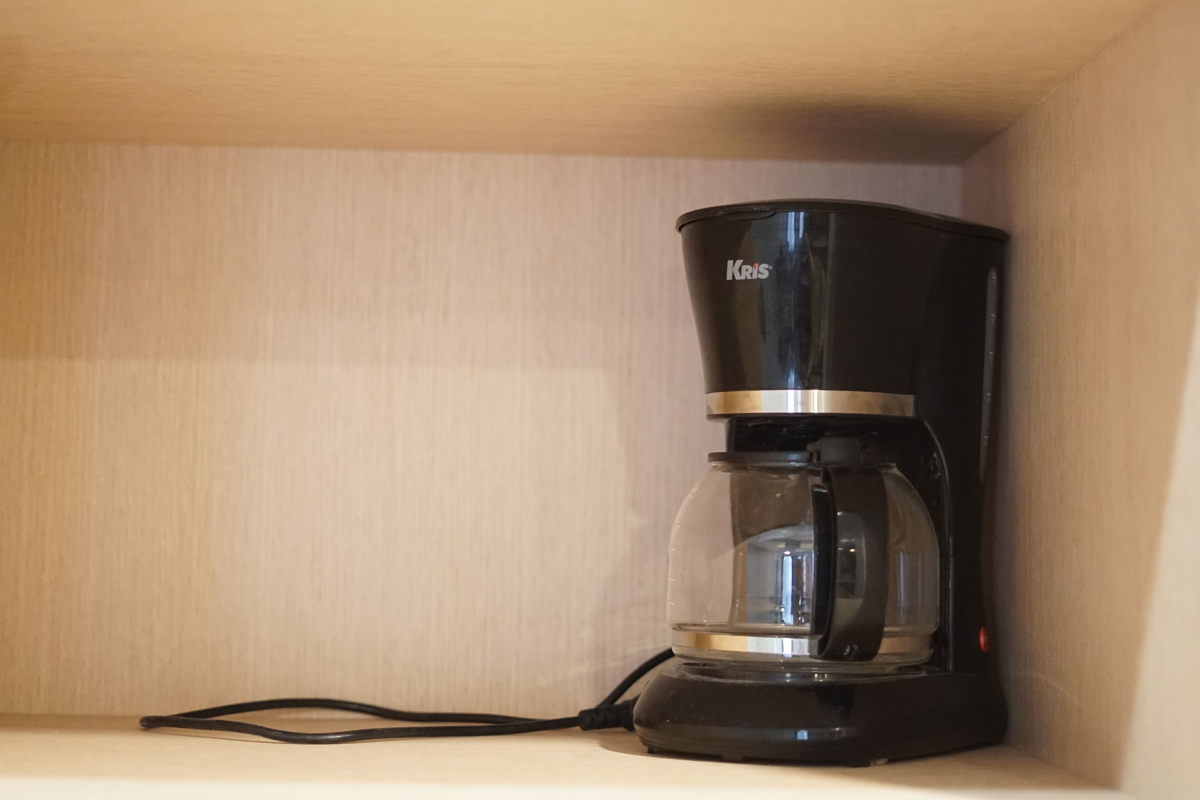 A black coffee maker with a glass carafe on a white shelf.