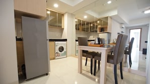 A modern kitchen with a built-in washing machine, a dining area with a table and chairs, and a refrigerator. - Apatel The Mansion Jasmine Aurora 31 I (Jakarta)
