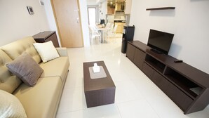 Una sala de estar moderna con un sofá, una mesa de centro, un televisor y una cocina al fondo.