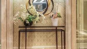 A marble reception area with a console table, a decorative mirror, and two wall-mounted lights. - Apatel Roseville SOHO & Suite (South Tangerang)