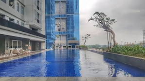 A modern hotel with a swimming pool, outdoor seating, and a view of the cityscape. - Apatel Roseville SOHO & Suite (South Tangerang)