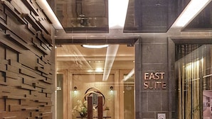 A modern hotel entrance with a brick wall, a sign for the East Suite, and a no-pet policy sign. - Apatel Roseville SOHO & Suite (South Tangerang)