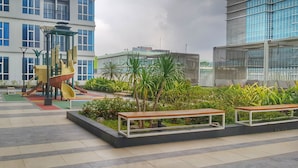 A rooftop playground with slides and a climbing structure, surrounded by benches and greenery. - Apatel Roseville SOHO & Suite (South Tangerang)