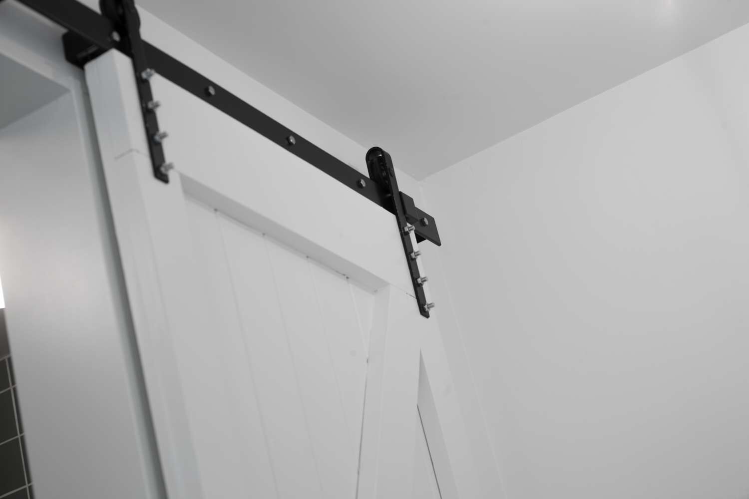 Une porte coulissante blanche avec un rail noir et un petit objet noir fixé à celle-ci.