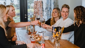 En grupp människor som skålar vid ett träbord med vinglas, ljus och en vas med blommor.