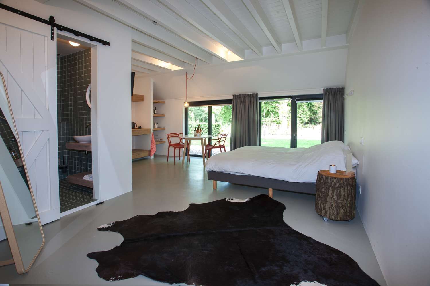 A modern bedroom with a large bed, a dining area, and a bathroom with a tiled shower.