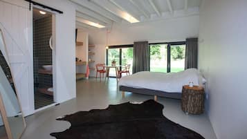 A modern bedroom with a large bed, a dining area, and a bathroom with a tiled shower.