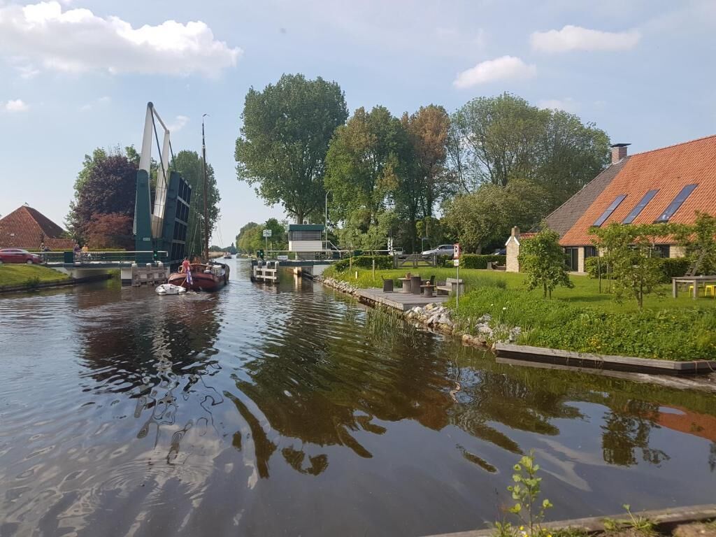 Un canal con un muelle para barcos, un edificio moderno de estructura singular, y casas residenciales con tejados inclinados.