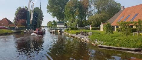 Un canal con un muelle para barcos, un edificio moderno de estructura singular, y casas residenciales con tejados inclinados.