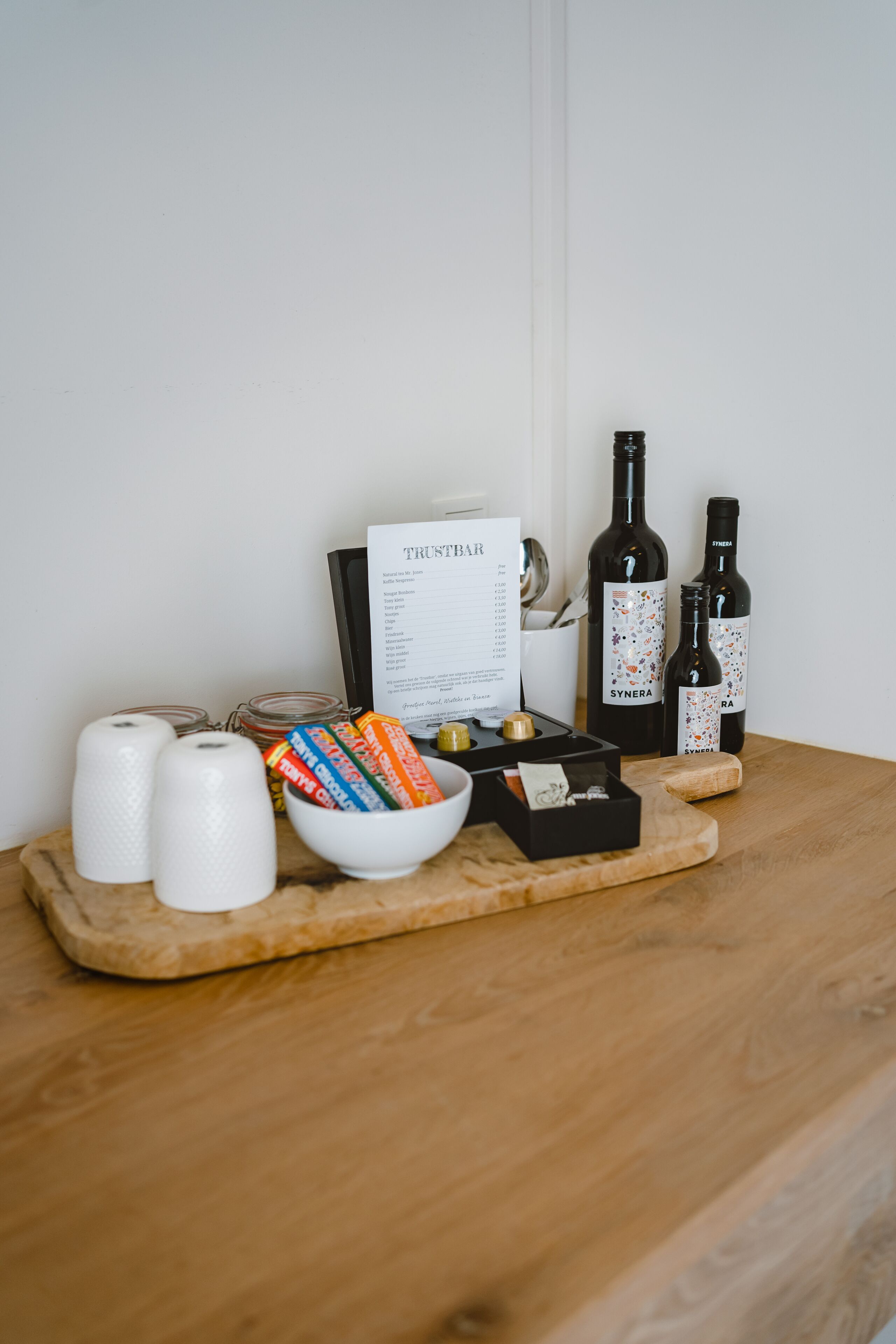 Una mesa de madera con un menú, dos botellas de vino, un bol de aperitivos y dos velas blancas.
