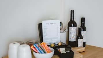 Una mesa de madera con un menú, dos botellas de vino, un bol de aperitivos y dos velas blancas.