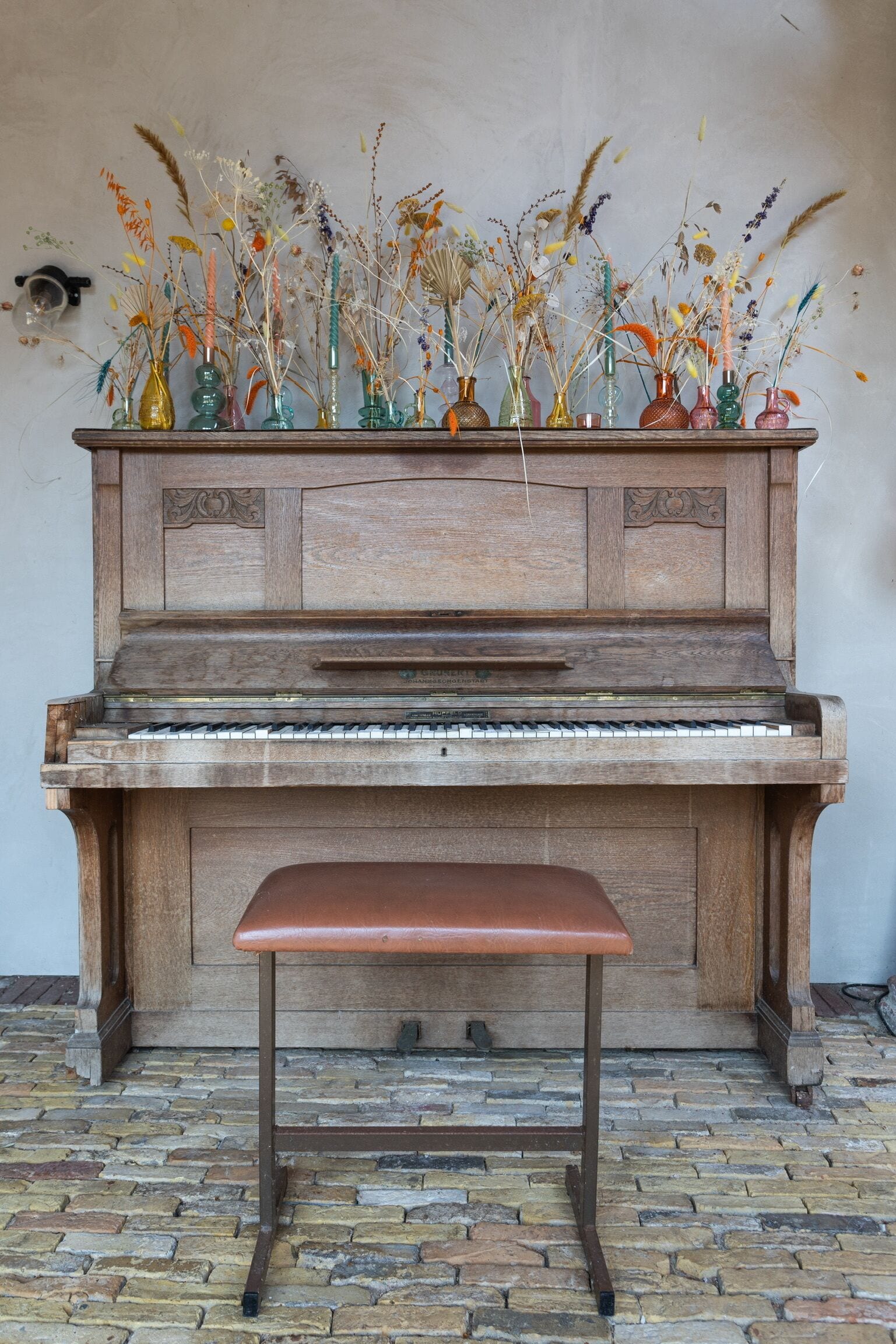 A wooden piano with a bench in front, placed on a cobblestone floor.