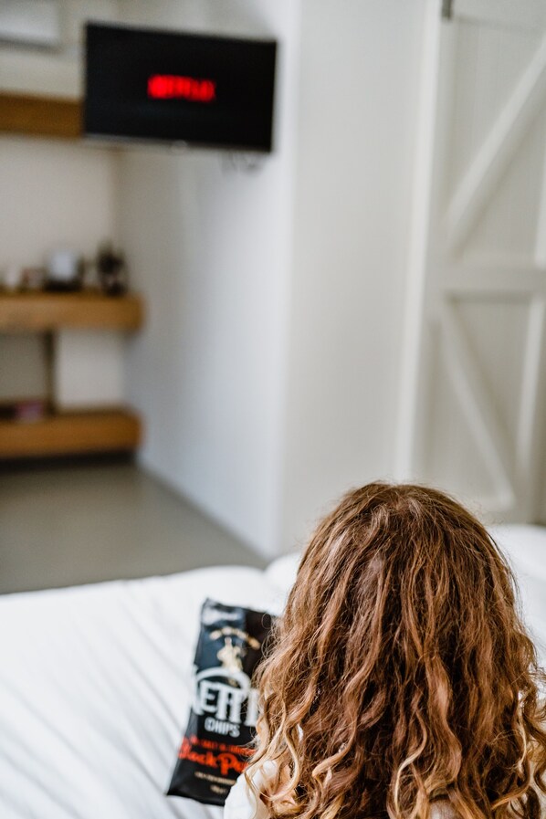 Un dormitorio con una cama, un almohadón, una bolsa de papas y un televisor en la pared.
