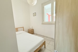 Ein Schlafzimmer mit Bett, Nachttisch, Lampe, Fenster und Tür.