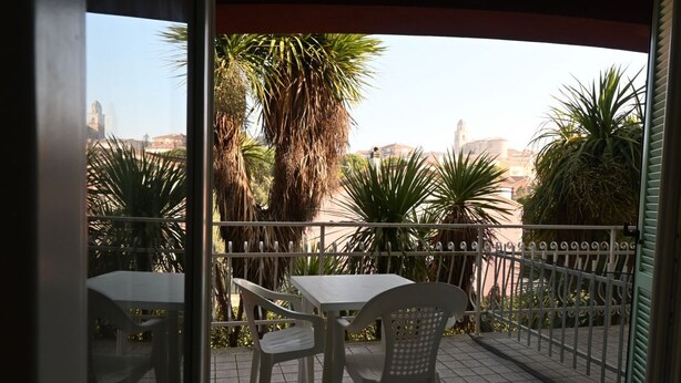 Ein Balkon mit Tisch und Stühlen, einem Metallzaun und Palmen.