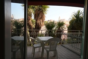 A balcony with a table and chairs, a metal fence, and palm trees. - S008 - Sirolo, new three-room apartment with terrace (Sirolo)