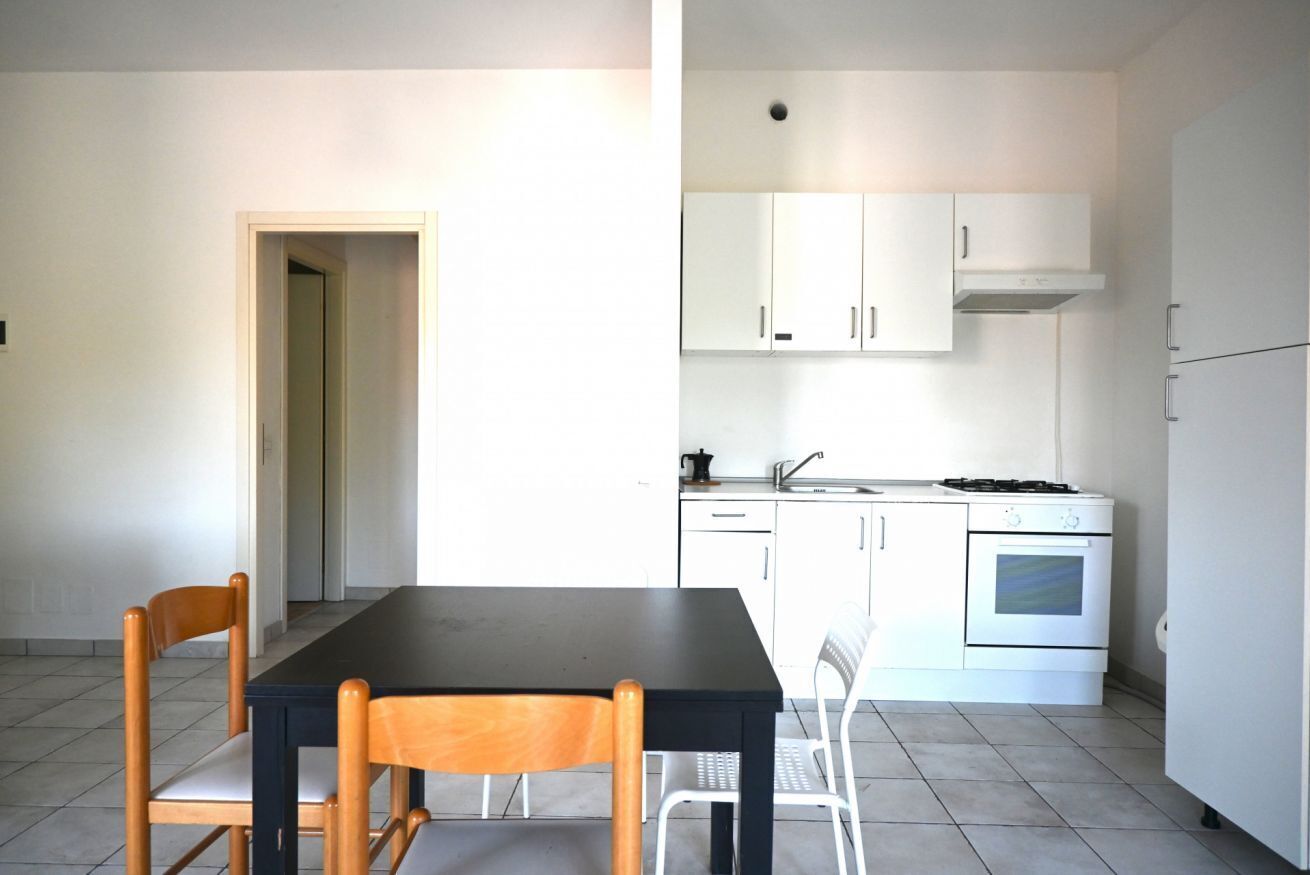 Een keuken met witte kastjes, een fornuis en een spoelbak. Er staat een eettafel met stoelen.