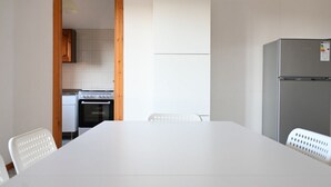 Una cocina con una mesa y sillas blancas, un refrigerador y un vano de madera que da a otra habitación.