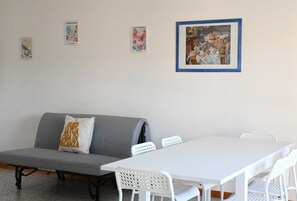 A room with a grey sofa, white chairs, a white table, and three framed artworks on the wall.