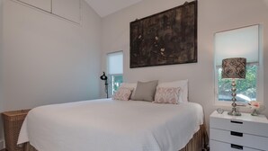 A bedroom with a large bed, a bedside table with a lamp, a window with blinds, and a painting on the wall. - Lido Beach Walk! One block to beach! (Sarasota)