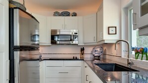 A compact kitchen with white cabinets, stainless steel appliances, a black countertop, and a decorative ceramic piece. - Lido Beach Walk! One block to beach! (Sarasota)