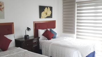 Habitación de hotel con dos camas, una mesita de noche, una lámpara, un cuadro y una ventana con persianas.