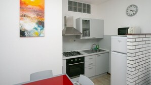 A compact kitchen with a gas stove, oven, and a microwave. There is a clock on the wall and a painting above the sink.