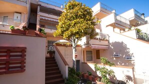 A multi-story residential building with balconies, potted plants, and a staircase leading to the upper floors.