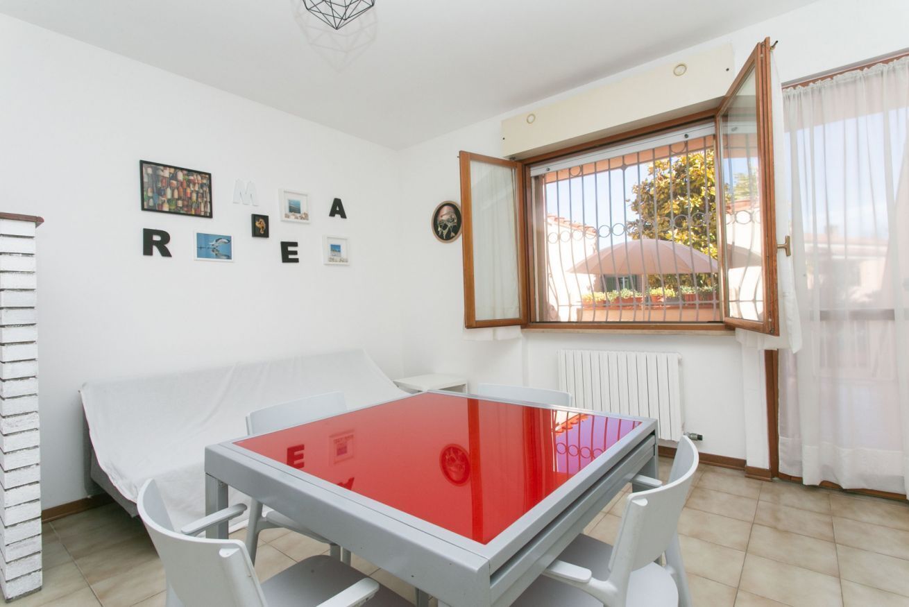A room with a bed, a table with a red top, a window with bars, and a wall with letters spelling 'REARE'.